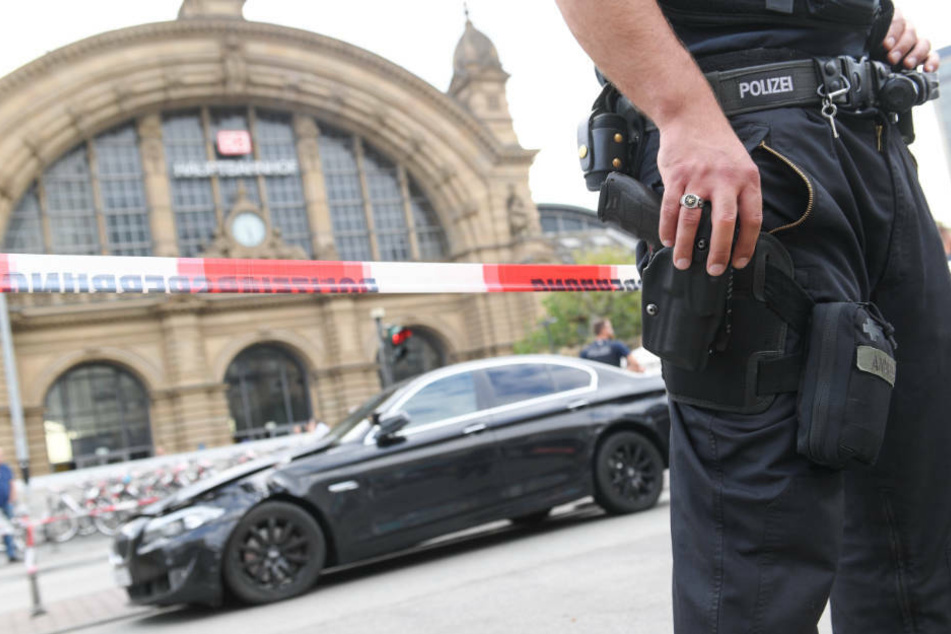 Ein Polizeibeamter steht am Frankfurter Hauptbahnhof vor einem schwarzen BMW, mit dem mehrere Täter dem Raubüberfall geflüchtet waren (Archivbild).
