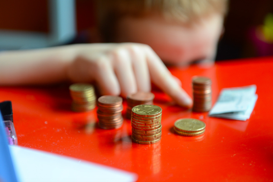 Ein Junge sitzt an einem roten Tisch und zählt Geld. (Symbolbild)