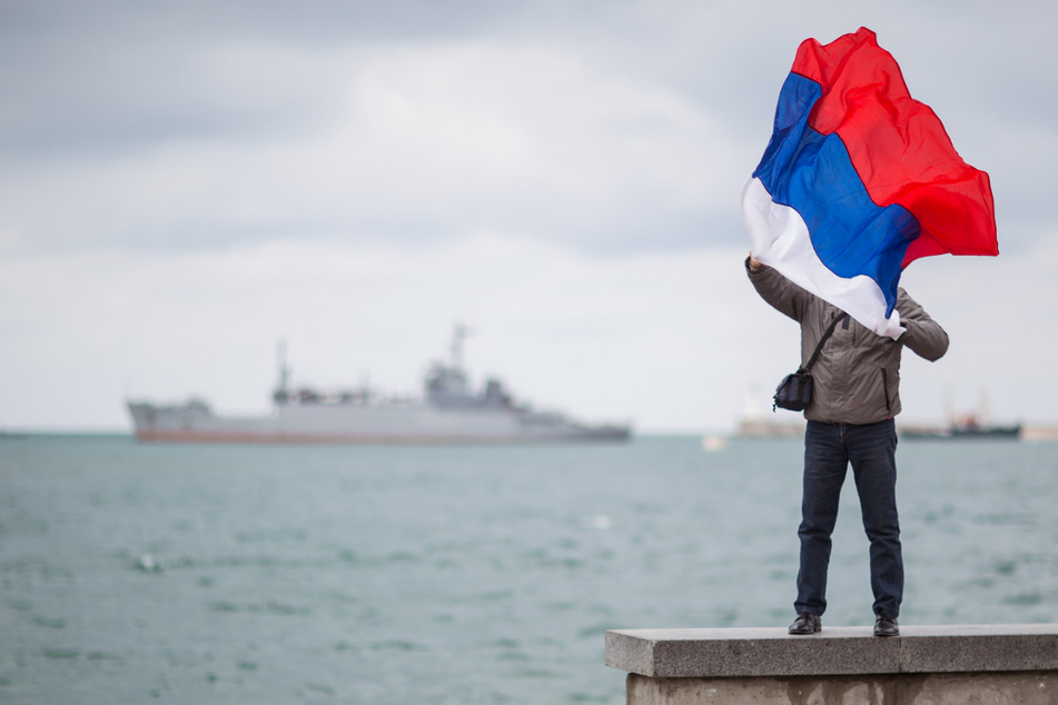 Ein Mann posiert mit einer Russland-Fahne an der Bucht von Sewastopol (Ukraine).