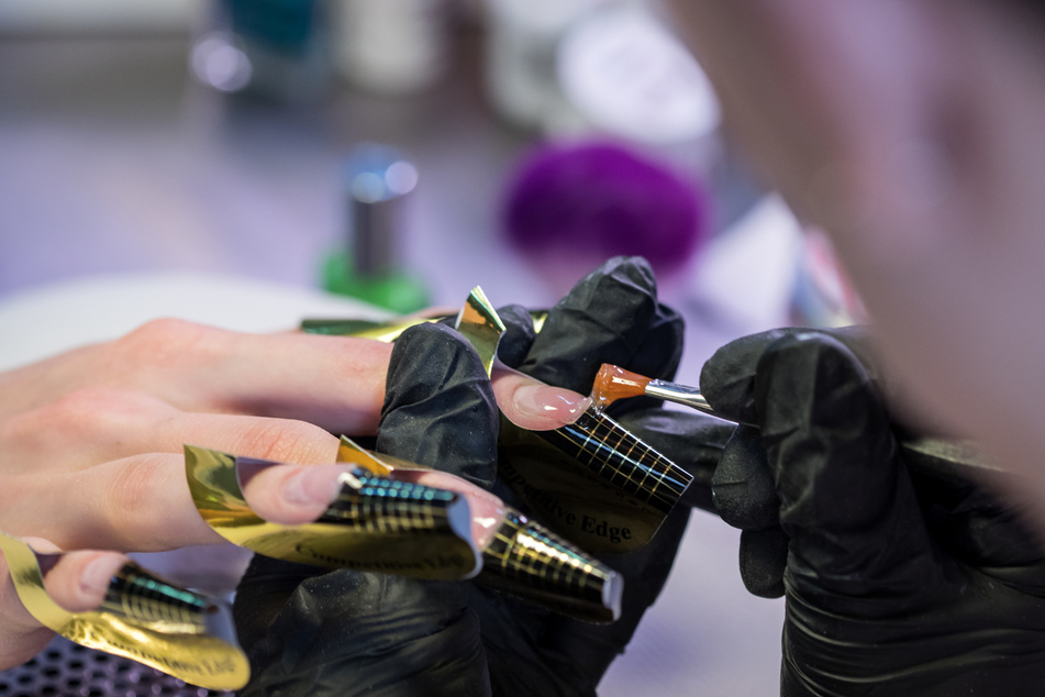 Eine Kosmetikerin trägt in einem Nagelstudio eine Gelschicht auf die Nägel einer Kundin auf.