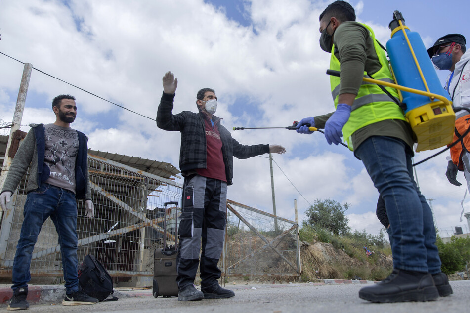 Ein Sanitäter des palästinensischen Gesundheitsministeriums desinfiziert palästinensische Arbeiter, als sie einen Kontrollpunkt der israelischen Armee verlassen.