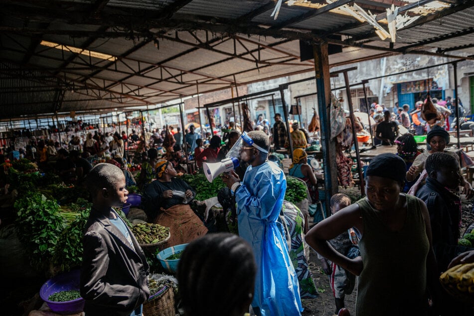 Menschen in Schutzkleidung betreiben auf einem Markt in Goma Aufklärungsarbeit als Teil der Maßnahmen zur Ebola-Prävention.