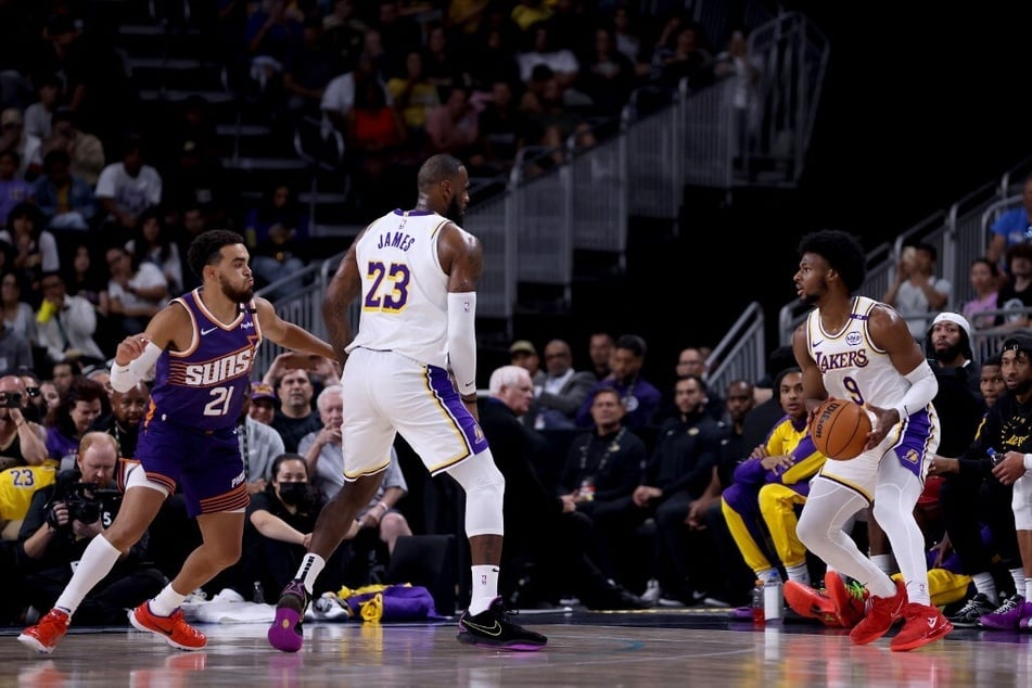 LeBron James (c.) of the Los Angeles Lakers sets a screen for Bronny James (r.) against Tyus Jones of the Phoenix Suns during the second quarter at Acrisure Arena.