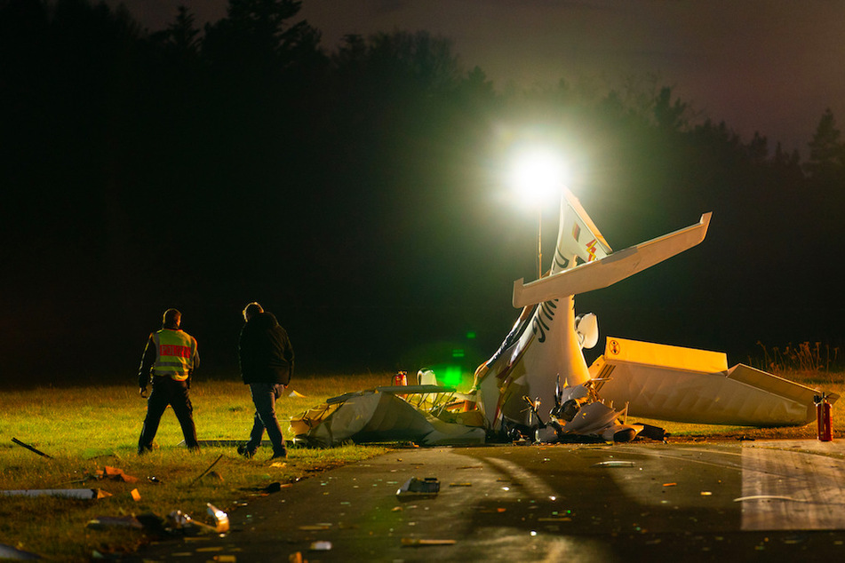 Einsatzkräfte stehen neben einem abgestürzten Sportflugzeug auf dem Rollfeld des Flugplatzes in Kulmbach.