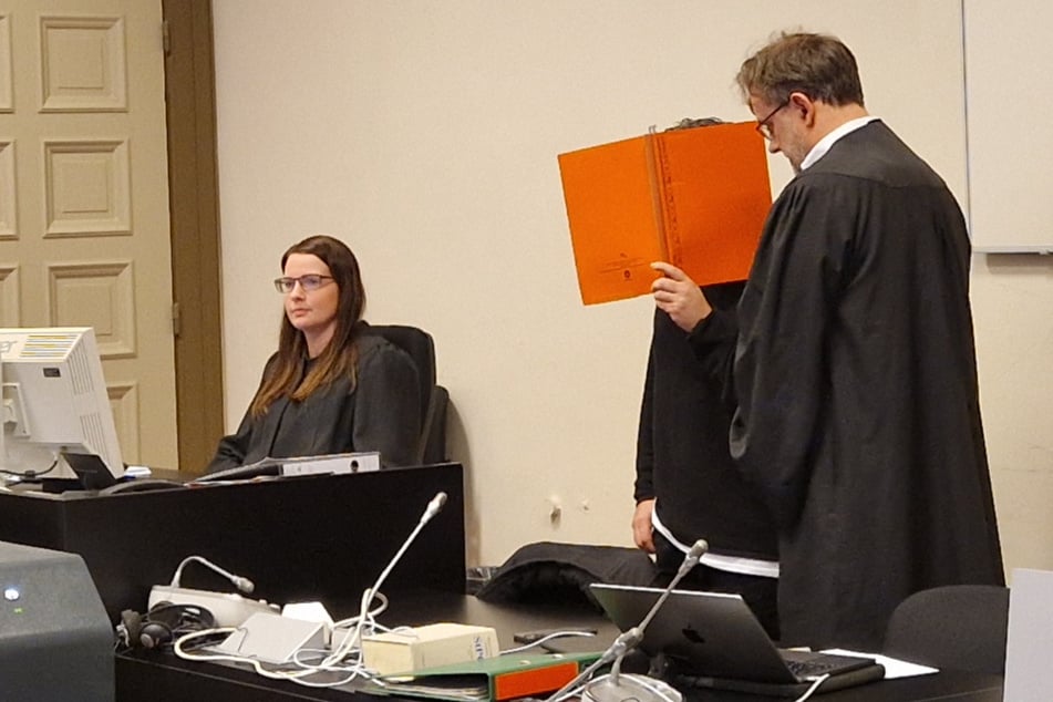 Der Angeklagte ließ sich beim Prozessauftakt am Donnerstag von einer roten Mappe und zusätzlich noch von seinem Anwalt verdecken.