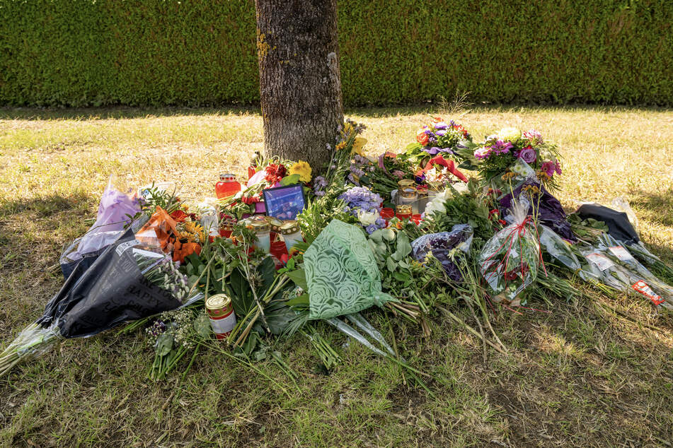 Blumen, Kerzen und Bilder liegen an einem Baum, in dessen Nähe im Augst 2022 eine weibliche Leiche in einem Auto entdeckt wurde.