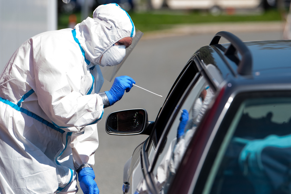 Ein Mann im Schutzanzug nimmt an einem Corona-Testzentrum einen Abstrich bei einem Autofahrer.