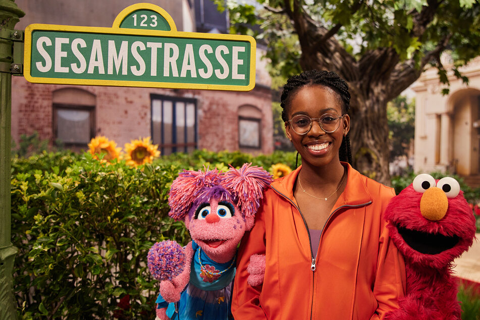 Die Weitspringerin Maryse Luzolo steht in einer Szene der "Sesamstraße" zwischen den Puppen Abby (l.) und Elmo.