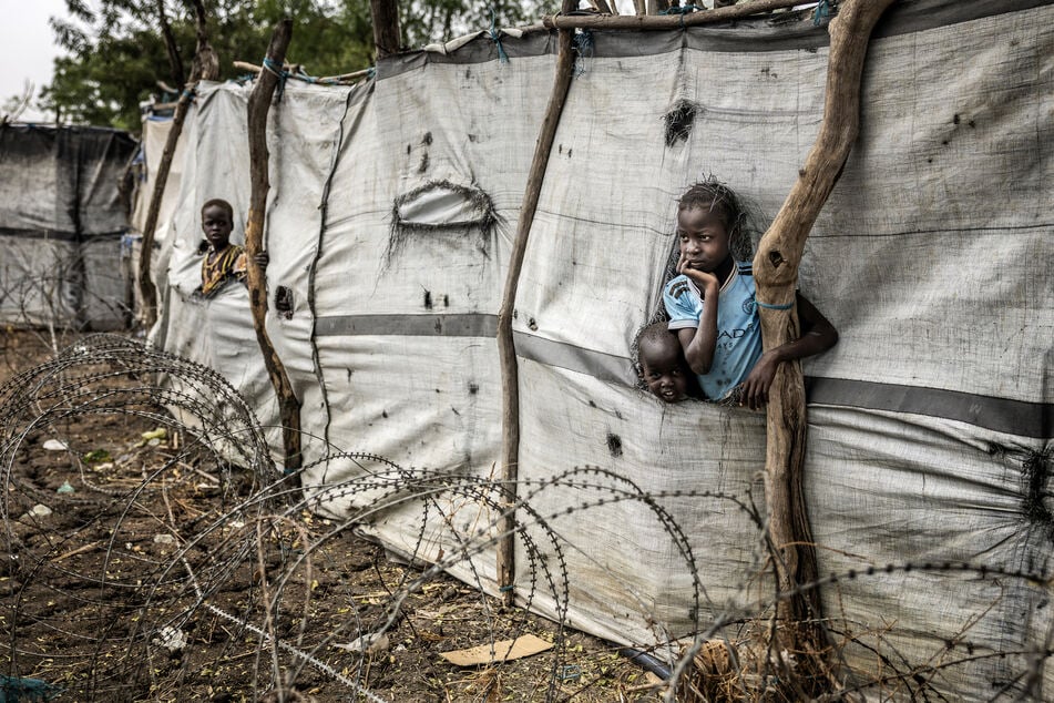 Children poke their heads and arms through holes in makeshift fabric fences in the strategic opposition-controlled town of Akobo, Jonglei State, on February 12, 2026.