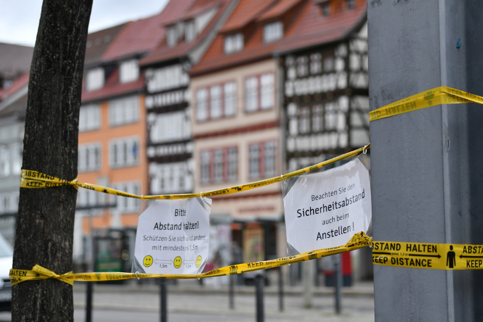 Zettel mit den Hinweisen "Bitte Abstand halten!" und "Beachten Sie den Sicherheitsabstand auch beim Anstellen!" sind mit Klebeband behelfsmäßig am Domplatz in Erfurt angebracht. (Symbolfoto)