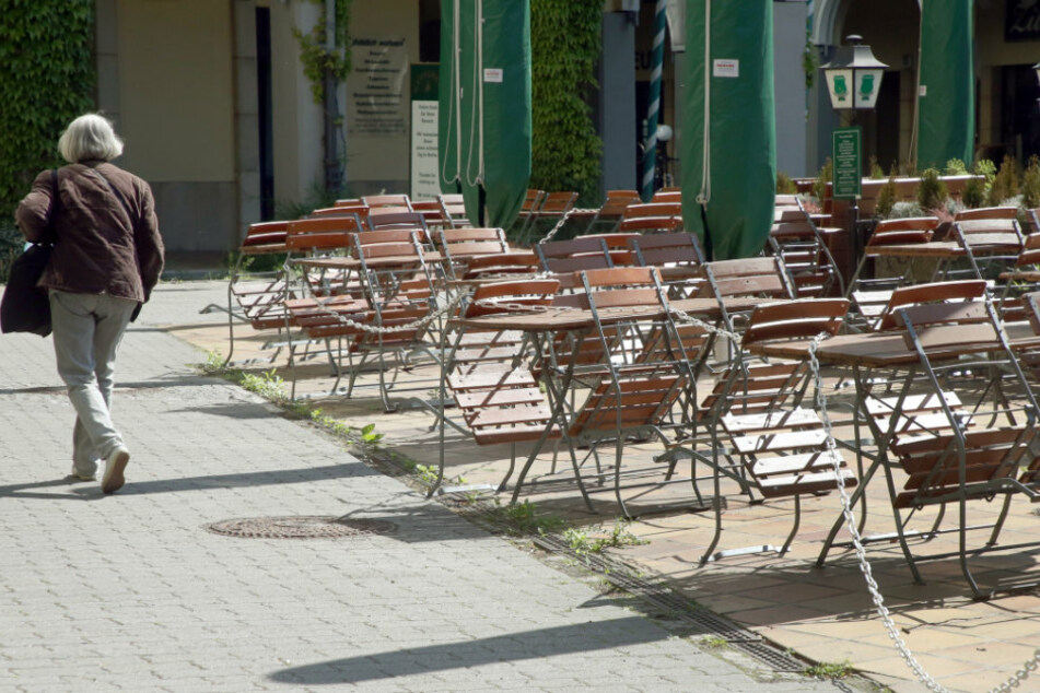Eine Frau geht im Nikolaiviertel an leeren Tischen und Stühlen eines geschlossenen Restaurants vorbei.