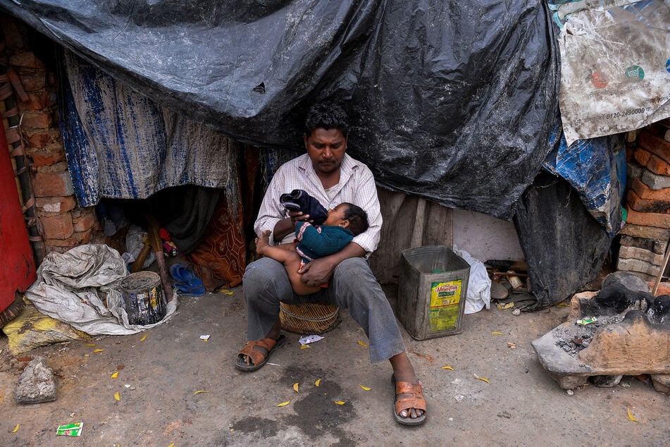 Ein Mann versorgt seine Tochter mit Flaschenmilch vor seinem provisorischen Zuhause in einem Elendsviertel von Neu-Delhi.
