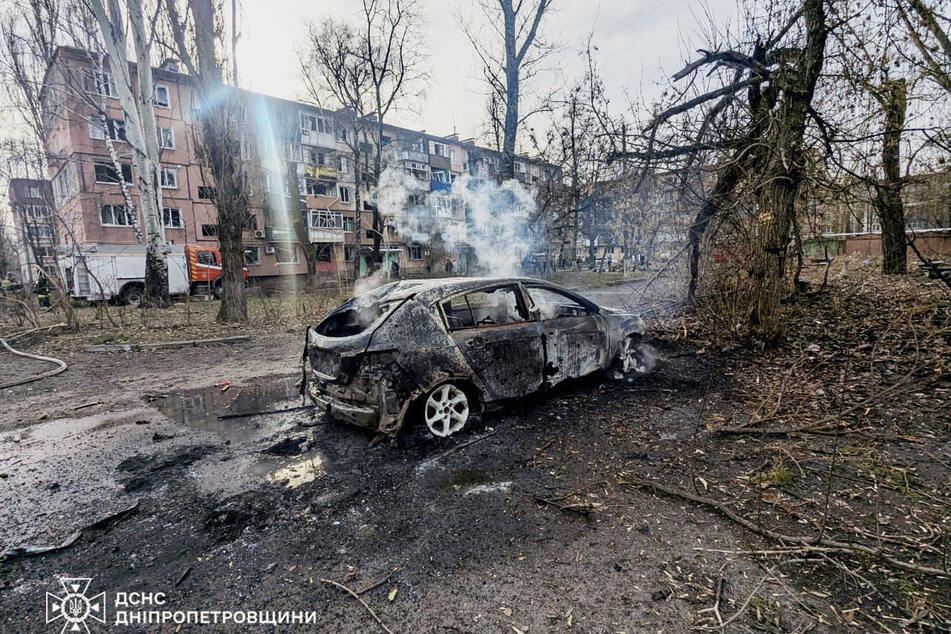 Auf diesem Foto der Stadt Krywyj Rih sind ein verbranntes Auto und beschädigte Wohnhäuser zu sehen, nachdem eine russische Rakete eingeschlagen ist.