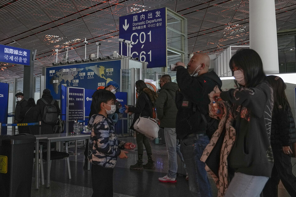 Passagiere stehen am Flughafen Peking an der Sicherheitskontrolle vor einem internationalen Abfluggate an.