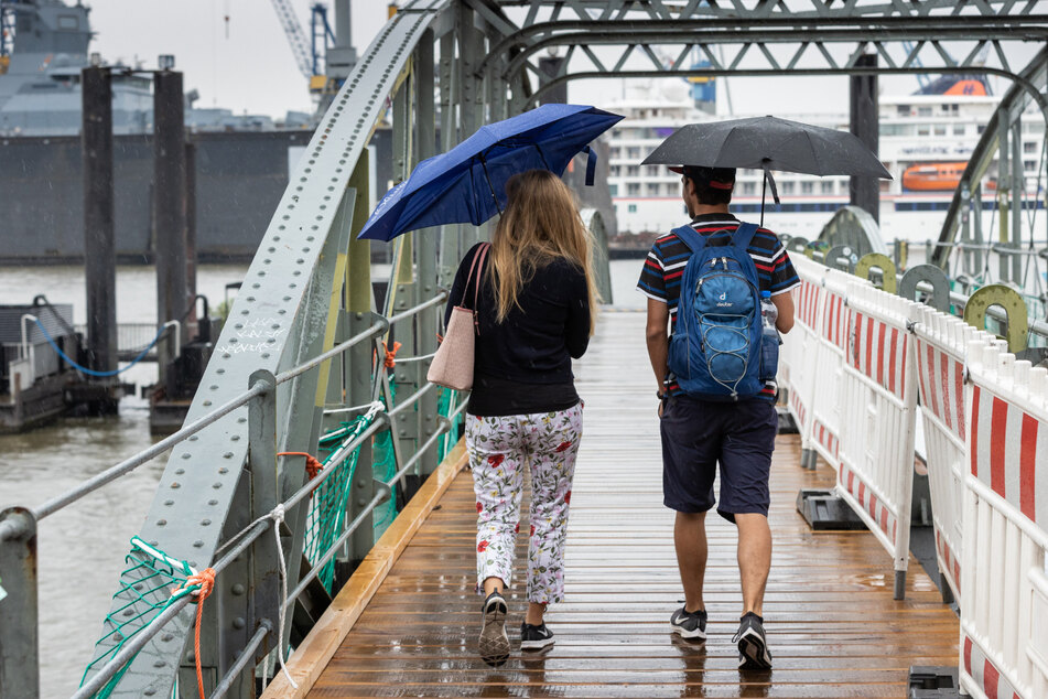 Mit Regenschirmen schützen sich eine Frau und ein Mann bei einem Spaziergang im Hamburger Hafen vor dem nassen Wetter.