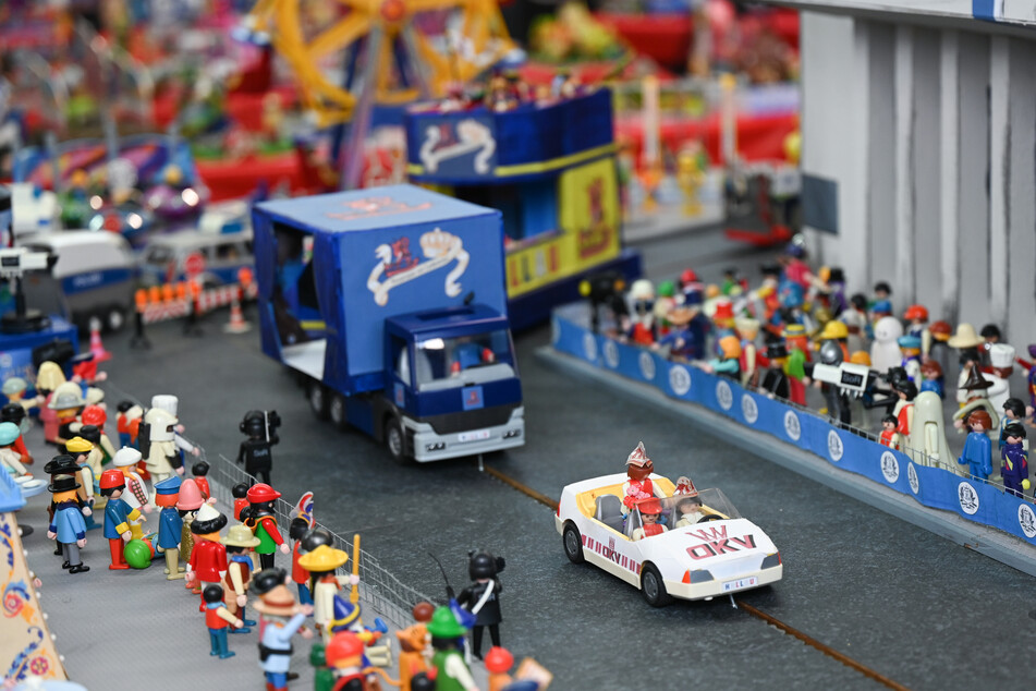 Playmobilfiguren und Miniatur-Motivwagen stellen einen Karnevalsumzug in einer nachgebauten Kulisse dar.