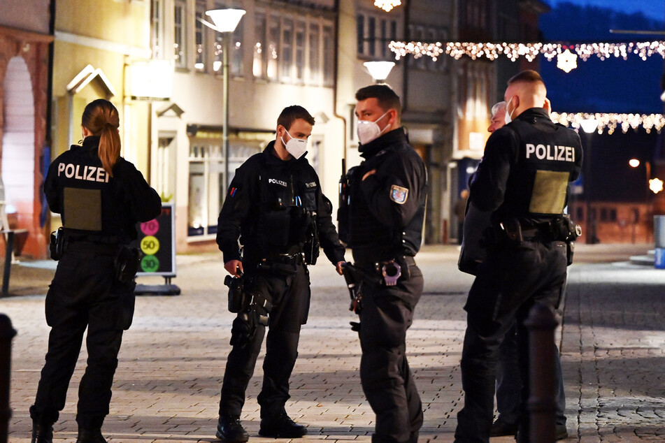 Polizisten stehen am Abend in einer Fußgängerzone und kontrollieren die neue Verordnung.