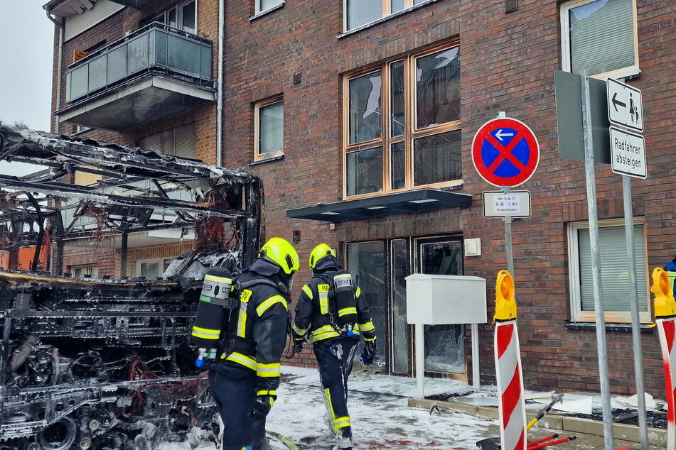 Feuerwehrleute vor dem völlig ausgebrannten Linienbus in Pinneberg. Auf der Straße ist der Löschschaum zu sehen.