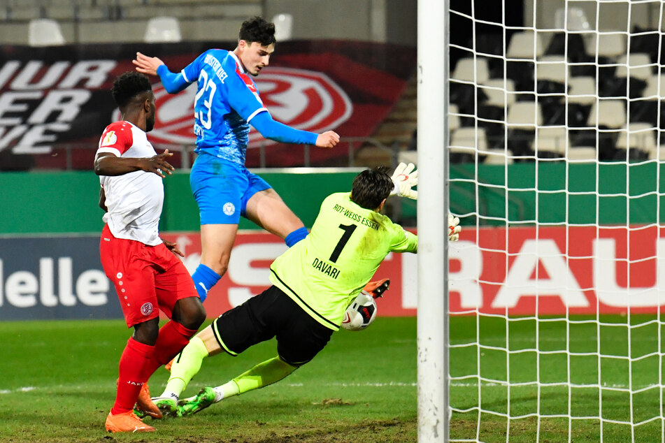 Janni Serra (M.) schießt den Ball unter dem herausstürzenden RWE-Keeper Daniel Davari (r.) zum 2:0 für Holstein Kiel ein.