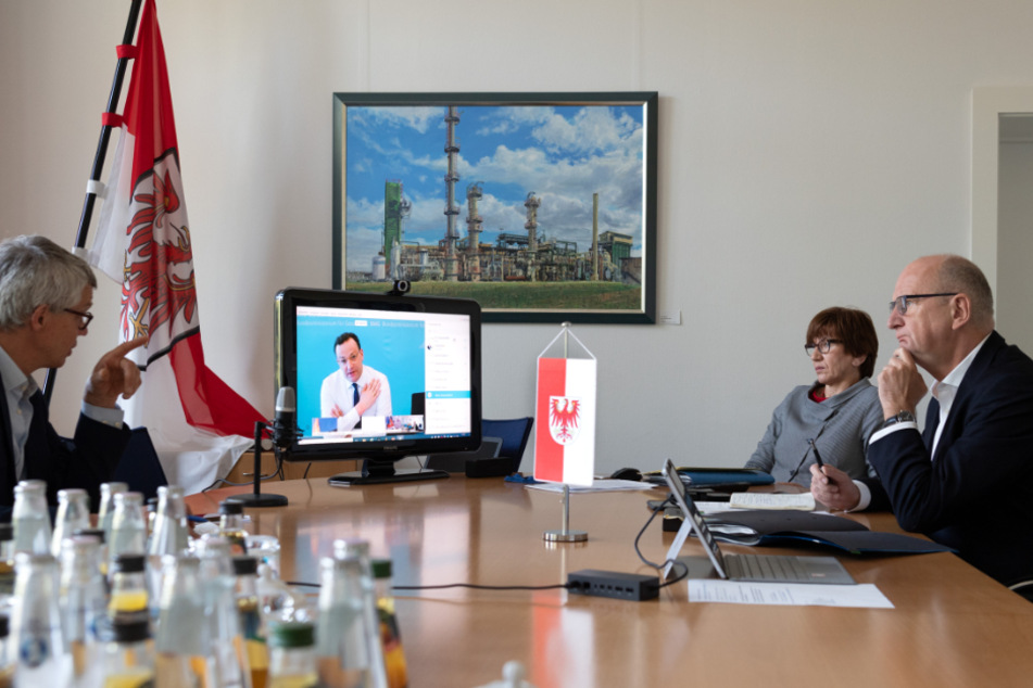 Dietmar Woidke (rechts), Ministerpräsident von Brandenburg, und Kathrin Schneider (beide SPD), Brandenburger Ministerin und Chefin der Staatskanzlei, verfolgen in der Staatskanzlei die Rede von Gesundheitsminister Jens Spahn (CDU) auf dem Monitor. Links sitzt der Brandenburger Regierungssprecher Florian Engels.