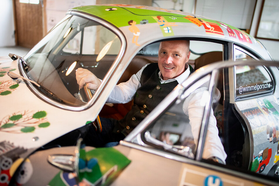 Helmut Freinecker, KFZ-Meister und Oldtimer-Experte, sitzt in seiner Werkstatt in seinem mit etlichen Wimmelbildern verzierten Porsche 356 B Super 90 Coupé.