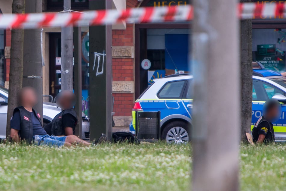Rocker der Hells Angels sitzen nach der Schießerei an Händen gefesselt auf einer Grünfläche. Gegen zwölf passiv Beteiligte sollen die Verfahren jetzt eingestellt werden.