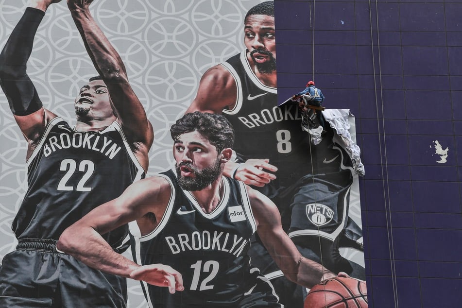 A worker removes a promotional banner from a building for the NBA preseason game in China between the Brooklyn Nets and the Los Angeles Lakers in Shanghai on October 9, 2019.
