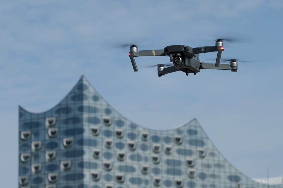 Eine Drohne, die mit einer Foto/Videokamera ausgestattet ist, schwebt in der Nähe der Elbphilharmonie am Himmel.
