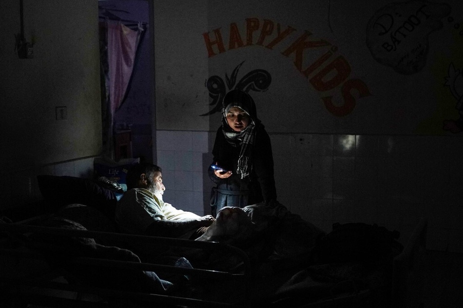 A woman uses a telephone torchlight as she stands next to a patient after a partial power cut at the Al-Aqsa Martyrs Hospital in Deir al-Balah.