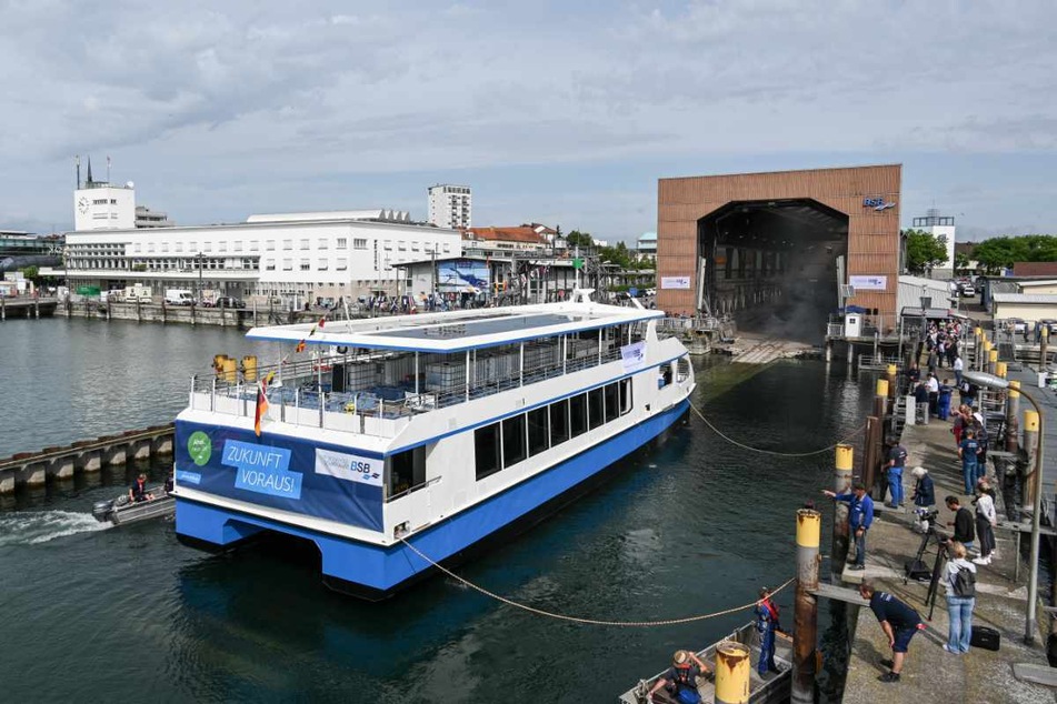 Friedrichshafen: Das erste vollelektrisch betriebene Schiff der Bodensee-Schiffsbetriebe (BSB) wird von der Werft ins Hafenbecken gelassen. Hunderte Menschen schauen beim Stapellauf des Katamarans zu.
