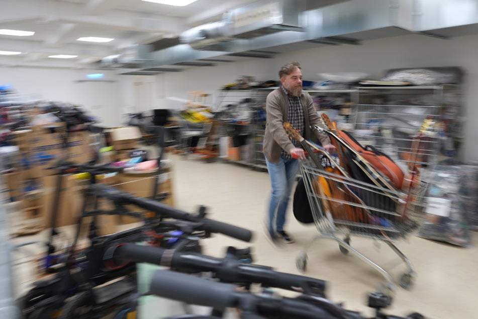 Richard Emmel schiebt einen Einkaufswagen mit abgegebenen Gitarren durch einen Lagerraum im Zentralen Fundbüro.