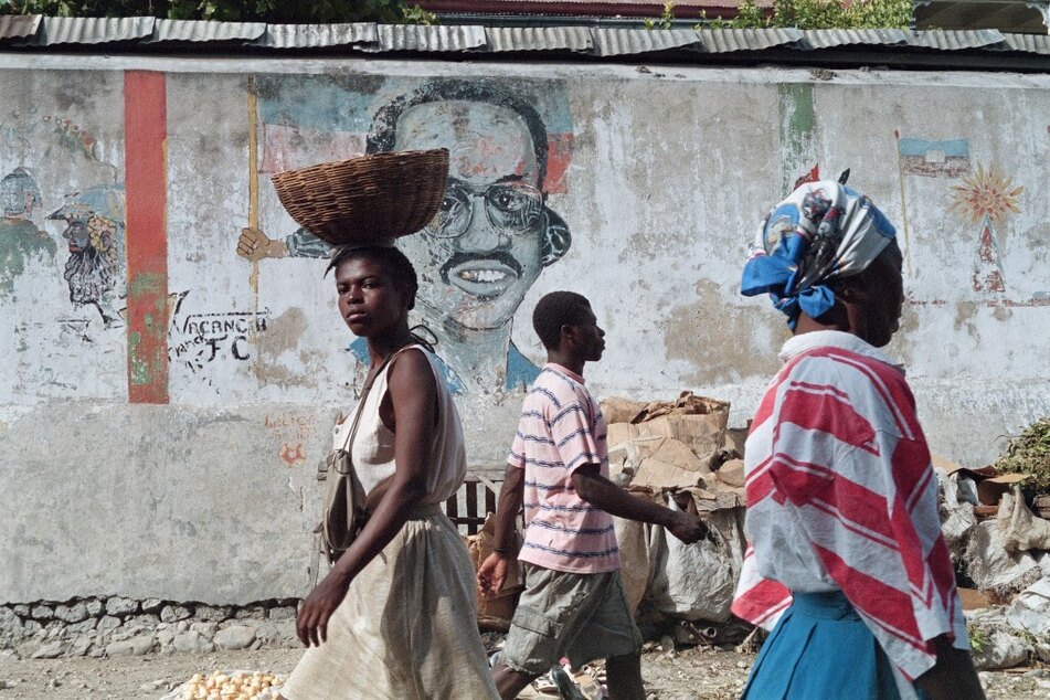 Haitians walk in front of a portrait of former Haitian President Jean-Bertrand Aristide, who alleged the US helped to orchestrate a coup to oust him, at the Port-au-Prince market.