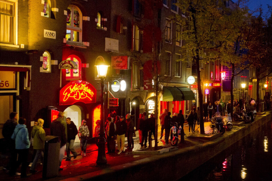 Menschen schlendern am Abend an einer Gracht entlang durch den Rotlichtbezirk De Wallen. (Archivbild)