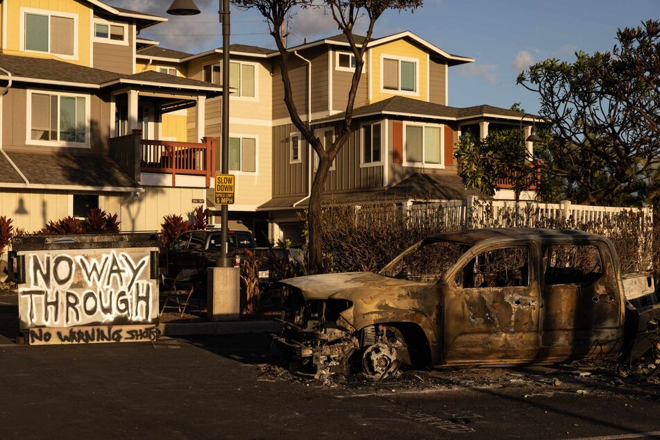 A burnt out car and a sign reading "No Way Through, No Warning Shots" stand in the driveway of a charred apartment complex in the aftermath of a wildfire in Lahaina, western Maui, Hawaii on Saturday. Hawaii's Attorney General Anne Lopez said she was opening a probe into the handling of devastating wildfires, as criticism grows of the official response.