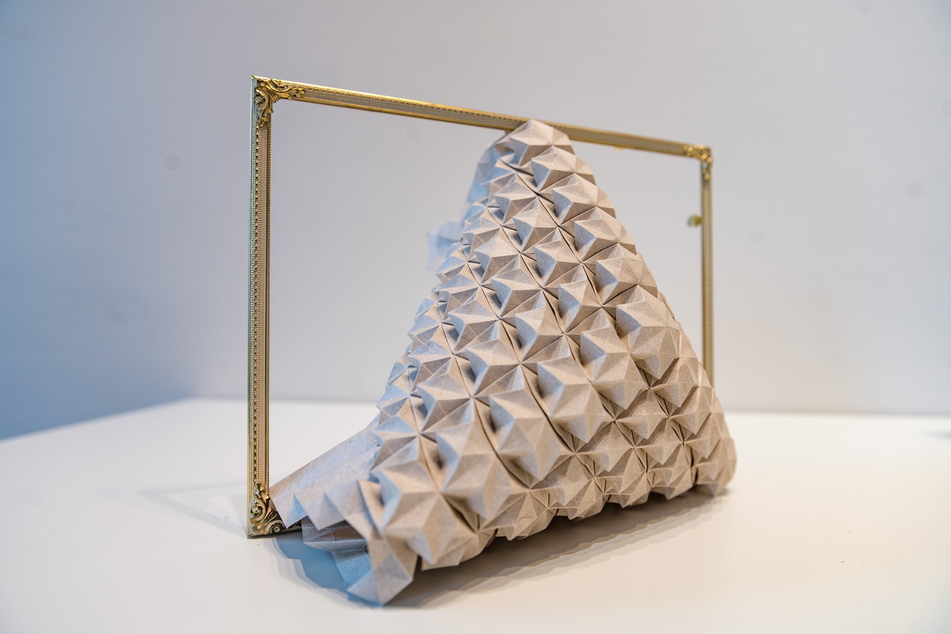 3D-Objektkunst aus Papier, die sich über ein Metallgestell schmiegt.