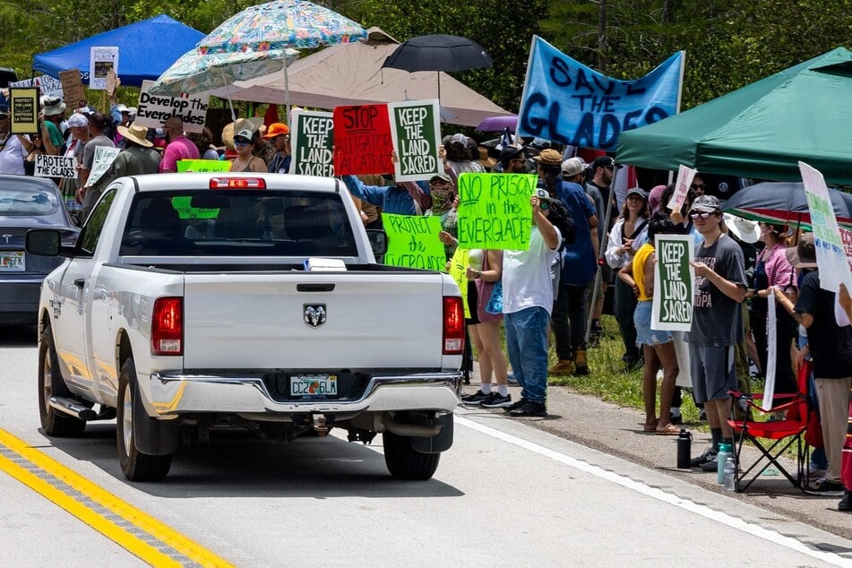 Cars drive past as Floridians raise signs opposing the construction of the Alligator Alcatraz immigrant detention center in the Everglades.