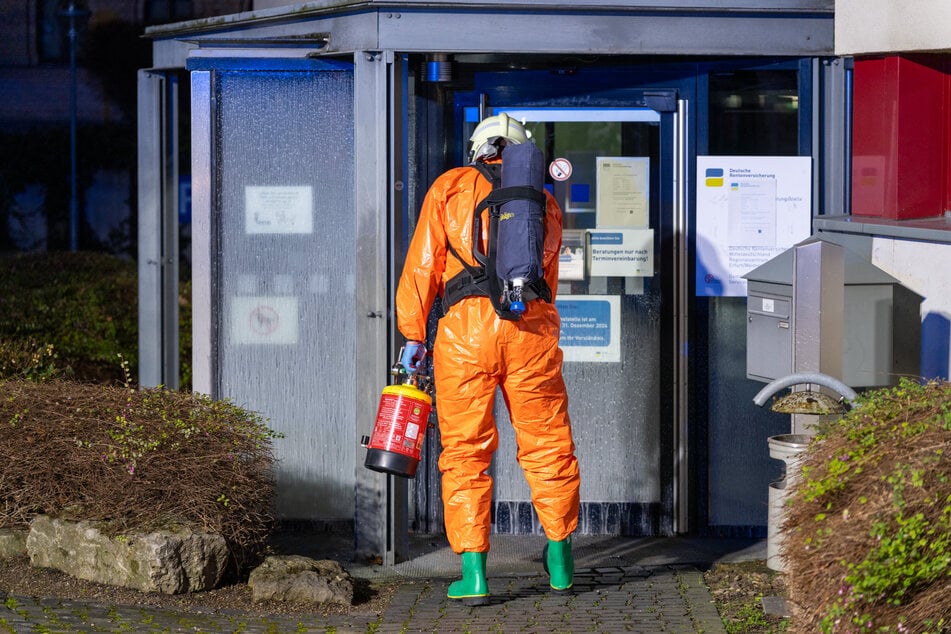 Ein Feuerwehrmann säuberte in Schutzausrüstung den Eingang der Rentenversicherung.