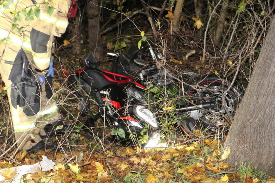 Ein Feuerwehrmann untersucht das völlig zerstörte Motorrad des verunglückten Fahrers, das neben einem Baum liegt.