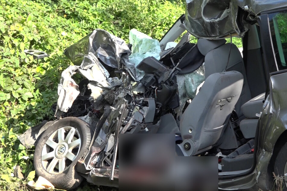 Die eingedrückte Fahrgastzelle eines PKw steht in einem Straßengraben der B211.