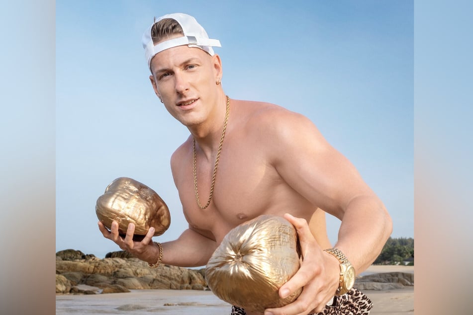 Calvin Kleinen (29) posiert mit zwei goldenen Kokosnüssen.