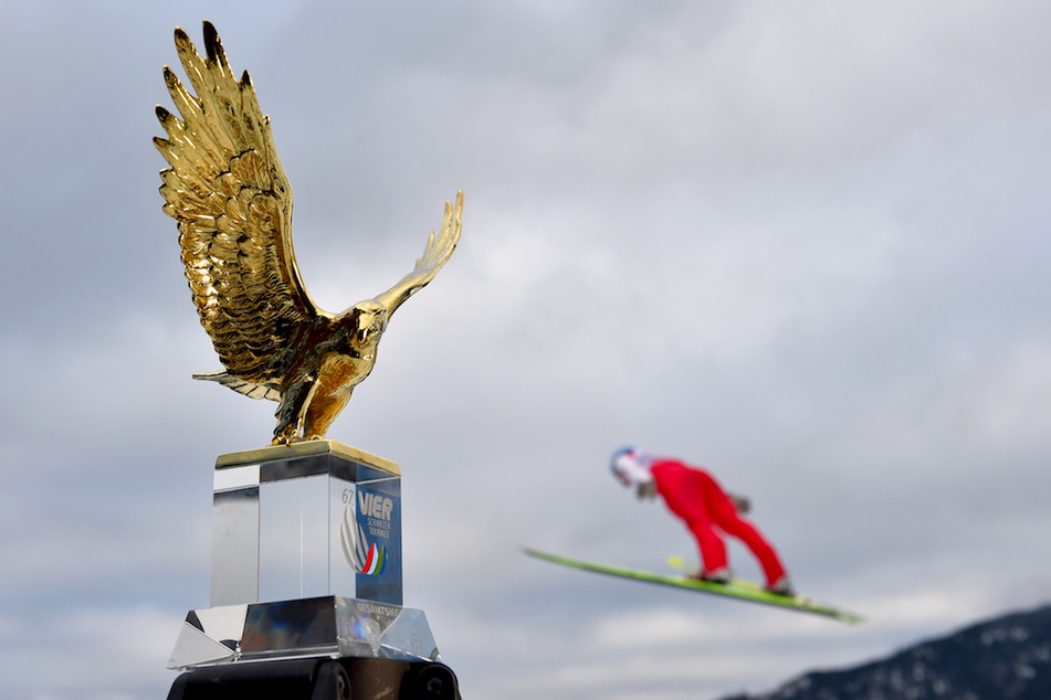 Ein Vorspringer springt hinter dem Pokal für den Gesamtsieger der Vierschanzentournee, dem goldenen Adler.