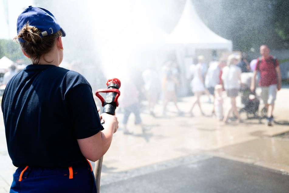 Eine Feuerwehrfrau sorgt mit einer Dusche aus dem Schlauch für etwas Abkühlung auf dem Hessentag.
