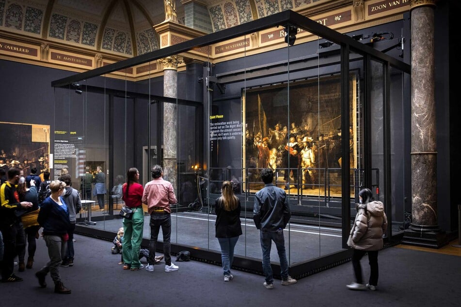 Visitors look at Rembrandt's Night Watch, which has been hung in place again after being stretched on an aluminum frame, at the Rijksmuseum in Amsterdam on March 16, 2022.