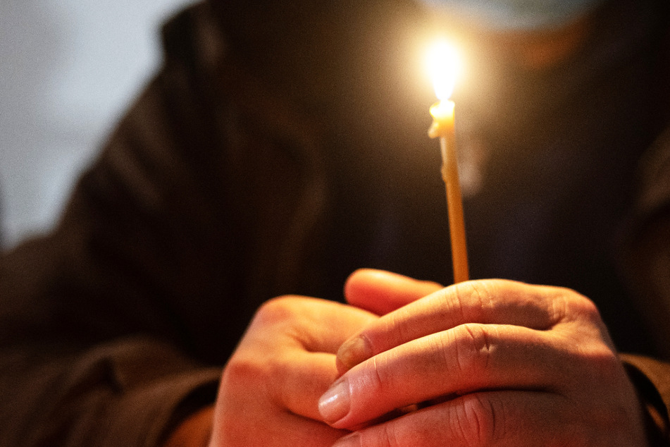 Ein Besucher sitzt während der "Langen Nacht am Heiligen Abend" mit einer Kerze beim Gottesdienst an einem Tisch - die Weihnachtsfeier fand in der Weißfrauen Diakoniekirche in Frankfurt statt.