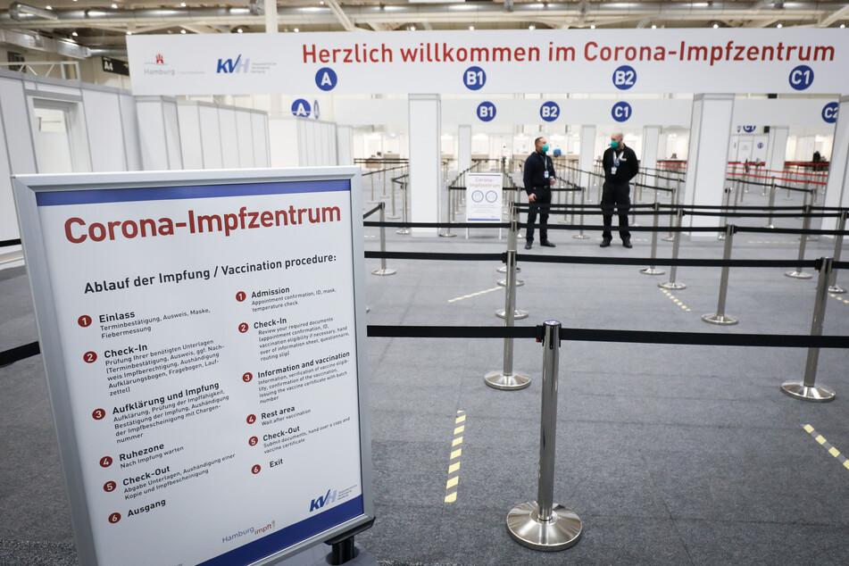 Zwei Mitarbeiter eines Sicherheitsdienstes stehen im Eingangsbereich des Corona-Impfzentrums in den Messehallen.