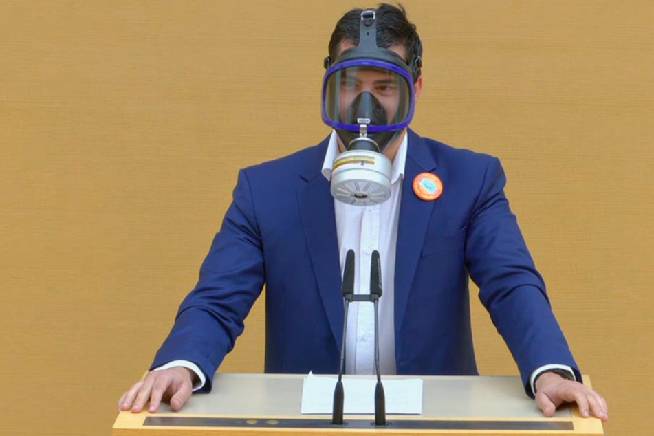 Der Screenshot aus einem Video zeigt den AfD-Abgeordneten Stefan Löw mit einer Gasmaske am Rednerpult im Bayerischen Landtag.