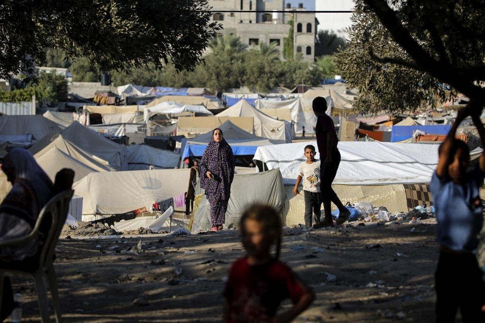 Children play as a woman walks near makeshift shelters at the al-Maghazi Palestinian refugee camp, in the central Gaza Strip.