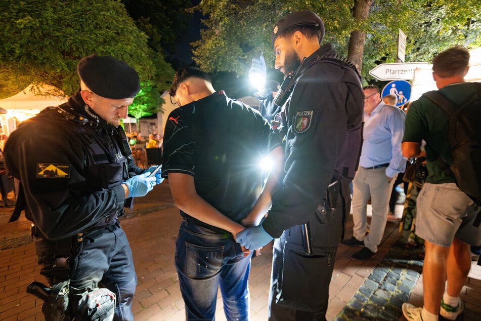 Einsatzkräfte der Polizei kontrollieren am späten Samstagabend einen Mann auf dem Jahrmarkt "Pützchens Markt". Ein anderer junger Mann wurde wegen eines Messers zuvor festgenommen.