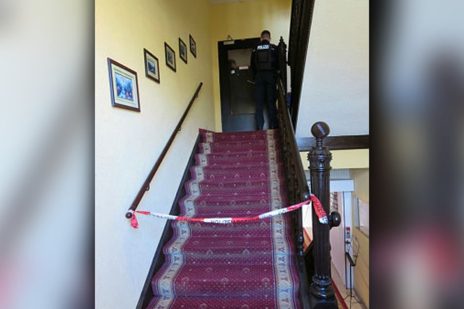 Die Po­li­zei hat den Auf­gang zum Ho­tel­flur der ers­ten Eta­ge ge­sperrt. Hin­ter die­ser Tür ge­schah ein schlim­mes Ver­bre­chen.