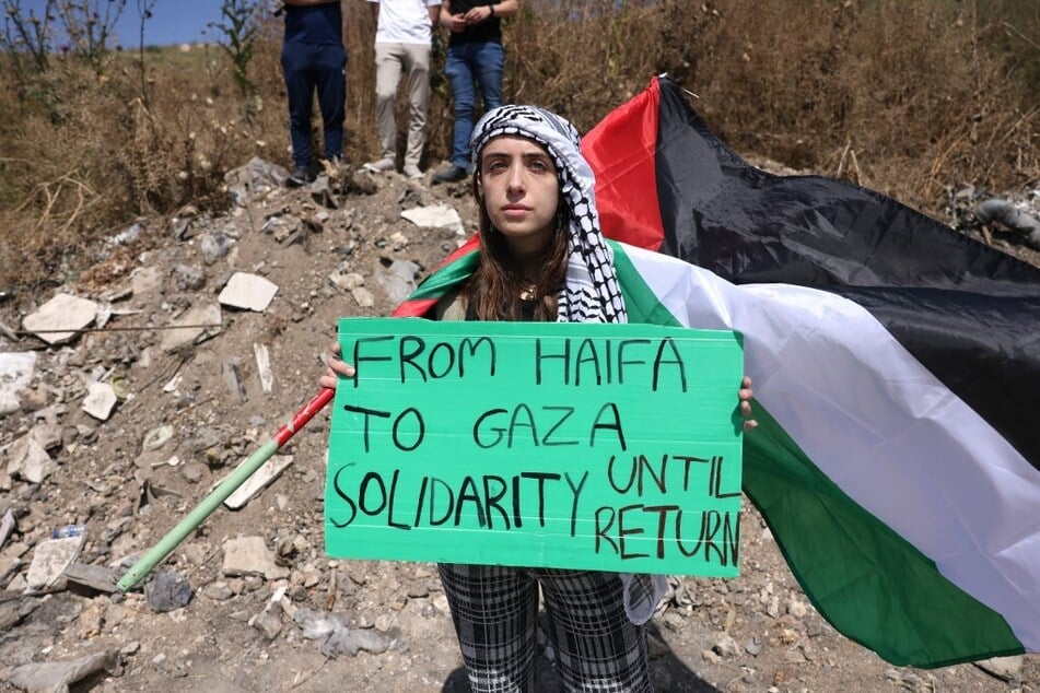 A woman holds a sign as Arab-Israeli protestors march with Palestinian national flags during a rally near Israel's northern city of Shefa Amr.